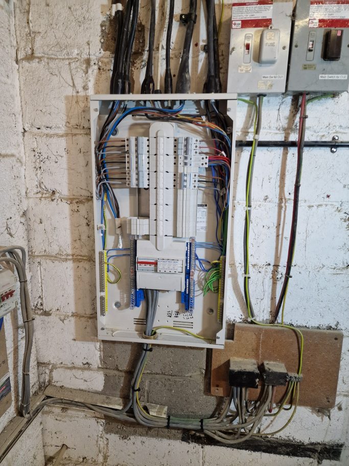 Old three‑phase consumer unit with poor cable terminations, poor cable positioning, and signs of thermal overload.